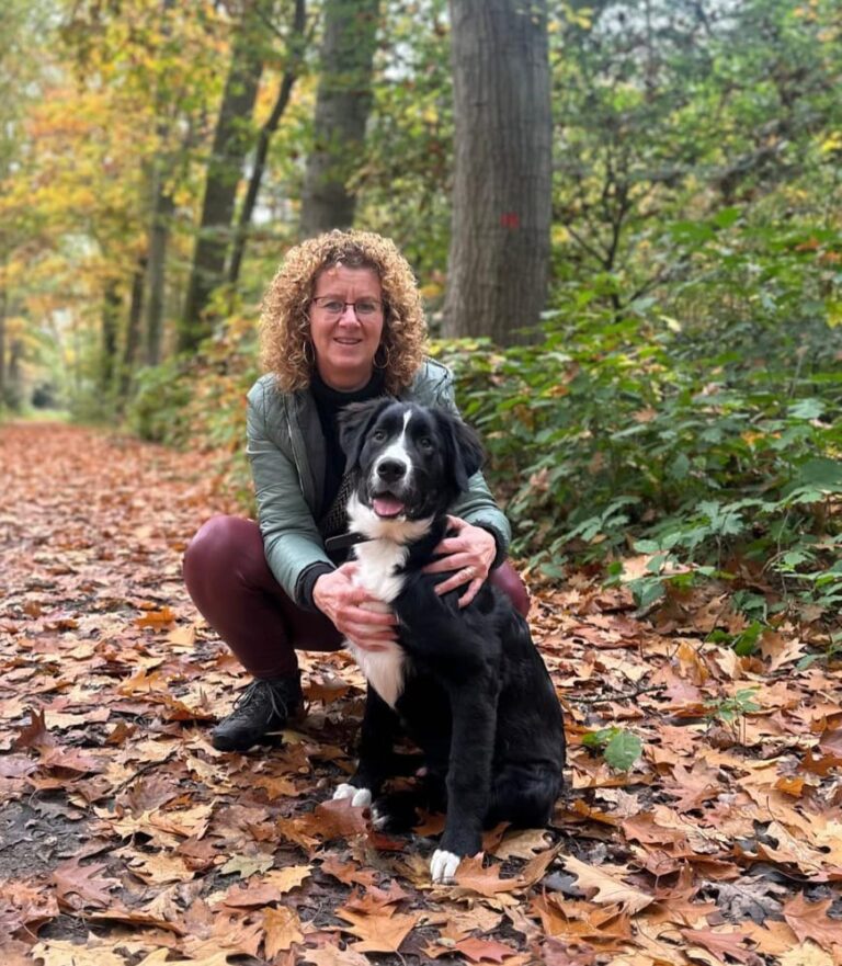 Gastouder Mariëlle zit met haar hond op een bospad vol herfstbladeren